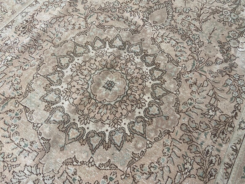 May include: Close-up of a vintage rug with a detailed floral pattern. The rug features a central medallion design in shades of brown, beige, and light green. The intricate pattern is visible across the entire surface, creating a textured appearance.