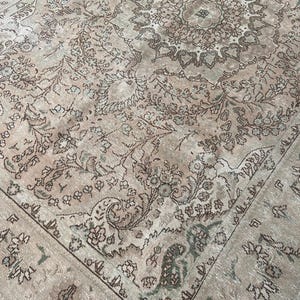 May include: A vintage area rug with an intricate floral pattern in shades of beige, brown, and green. The rug features a central medallion design and a detailed border. The rug's distressed appearance adds to its antique charm.