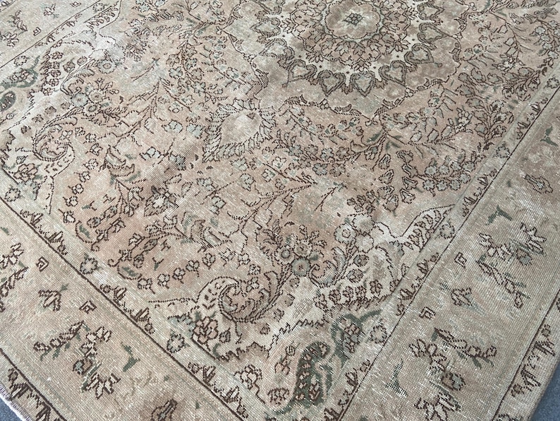 May include: A vintage area rug with an intricate floral pattern in shades of beige, brown, and green. The rug features a central medallion design and a detailed border. The rug's distressed appearance adds to its antique charm.