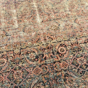 May include: An antique rug with a distressed, faded appearance. The rug features a complex, repeating pattern in shades of red, brown, blue, and cream. The design includes floral and geometric elements, creating a vintage aesthetic. The rug's texture appears worn.