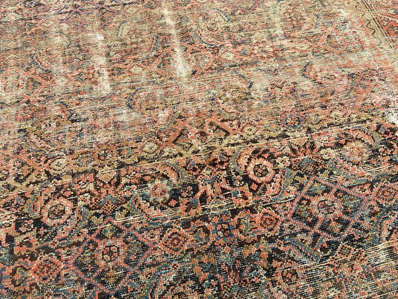May include: An antique rug with a distressed, faded appearance. The rug features a complex, repeating pattern in shades of red, brown, blue, and cream. The design includes floral and geometric elements, creating a vintage aesthetic. The rug's texture appears worn.