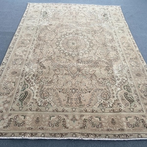May include: A rectangular, beige-toned rug with an intricate, floral-inspired central medallion design. The rug features a detailed border with repeating floral patterns and a faded, vintage aesthetic. The rug is placed on a blue surface.