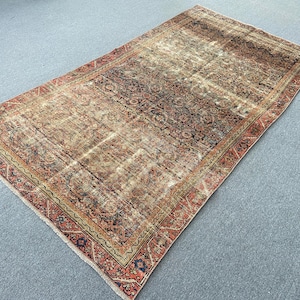 May include: A rectangular, distressed rug with a central field of brown and beige tones. The rug features a detailed, faded floral pattern and a border in shades of red, navy, and gold. The rug's design suggests a vintage or antique style.