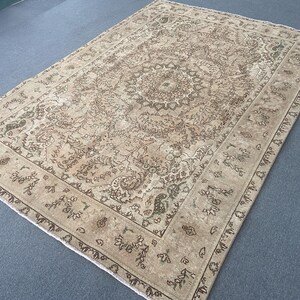 May include: A rectangular, beige-toned rug with an intricate, floral-inspired central medallion design. The rug features a detailed border with repeating patterns in shades of brown and green. The overall aesthetic is vintage and ornate.