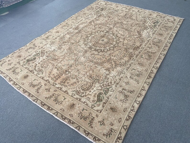 May include: A rectangular, beige-toned rug with an intricate, floral-inspired central medallion design. The rug features a detailed border with repeating patterns in shades of brown and green. The overall aesthetic is vintage and ornate.