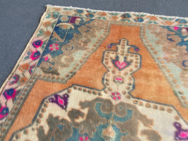 May include: A rectangular area rug featuring a central orange field with a large, intricate geometric medallion in shades of blue, brown, and cream. The border displays floral motifs in vibrant pink, deep blue, and green with a fringed edge.