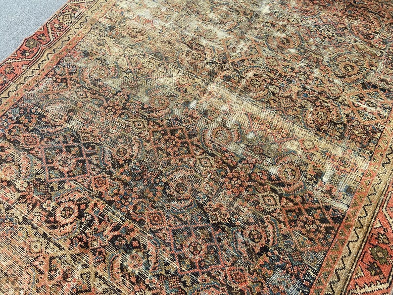 May include: An antique rug with a distressed, faded appearance. The rug features a complex pattern of geometric and floral designs in shades of red, black, and beige. The edges are bordered with a detailed pattern. The rug appears to be worn.