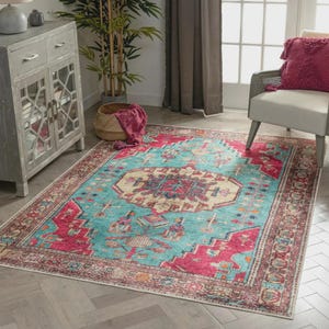 Puede incluir: Una alfombra rectangular con un diseño desgastado de inspiración vintage. La alfombra presenta un campo central turquesa con un patrón geométrico detallado en tonos de rojo, beige y marrón. El borde es de un rojo más oscuro con detalles intrincados.