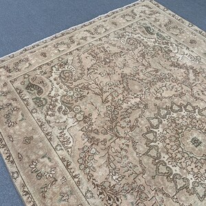May include: A rectangular, vintage-style rug with an intricate floral and geometric pattern. The rug features a beige background with brown and green accents, creating a warm and inviting aesthetic. The detailed design includes a central medallion and border.