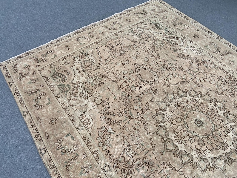 May include: A rectangular, vintage-style rug with an intricate floral and geometric pattern. The rug features a beige background with brown and green accents, creating a warm and inviting aesthetic. The detailed design includes a central medallion and border.