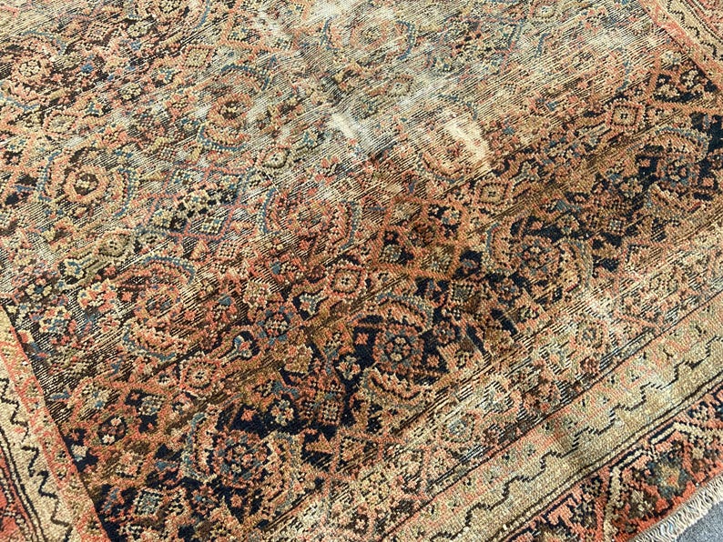 May include: An antique Persian rug with a detailed, faded floral pattern in shades of rust, navy, and beige. The rug's design features intricate medallions and borders, showcasing a vintage aesthetic.