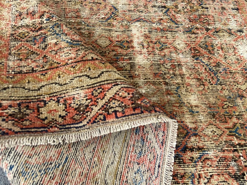 May include: A distressed, vintage-style rug with a detailed, repeating pattern. The rug features a color palette of muted reds, blues, and tans, with a fringed edge. The design has an aged, worn appearance, suggesting it is an antique or a reproduction.