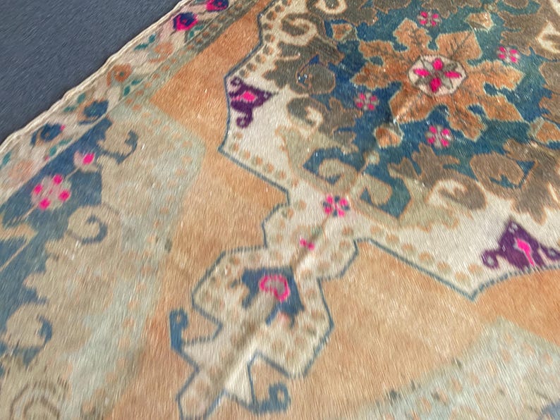 May include: A woven rug featuring a large central medallion in deep blue and brown tones, surrounded by a light orange field. The design includes intricate floral motifs and geometric borders accented with vibrant pink and purple details.