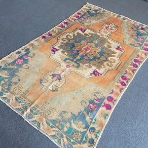 May include: A rectangular area rug featuring a central medallion in shades of blue, brown, and cream set against a vibrant orange background. The border displays a repeating floral pattern in pink, blue, and cream with a fringed edge on the ends.