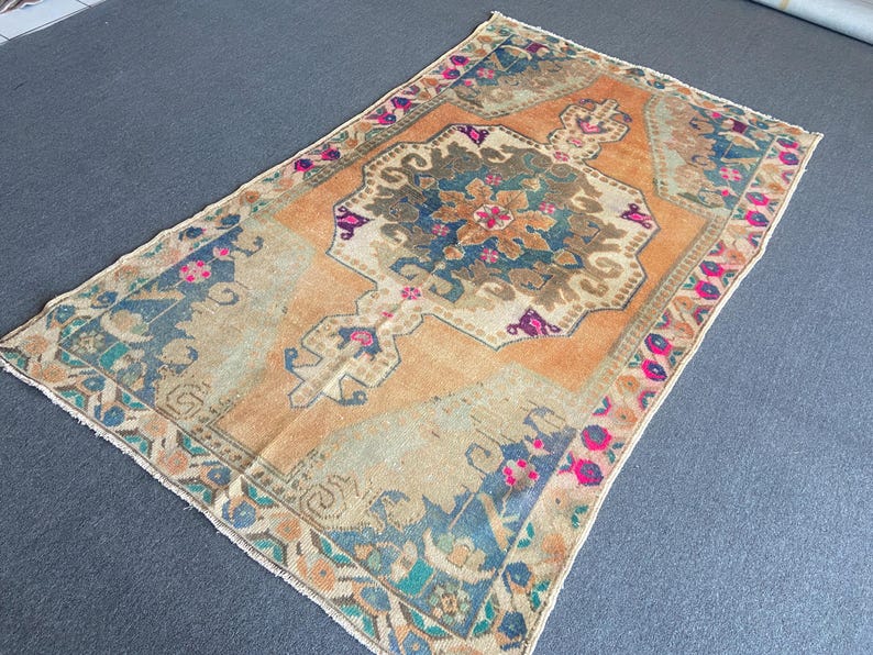 May include: A rectangular area rug featuring a central medallion in shades of blue, brown, and cream set against a vibrant orange background. The border displays a repeating floral pattern in pink, blue, and cream with a fringed edge on the ends.