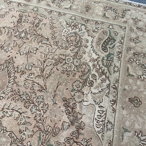 May include: A vintage-style rug with a faded, distressed appearance. The rug features a beige and brown color palette with intricate floral and paisley patterns. The border has a darker brown design, adding contrast to the overall look.