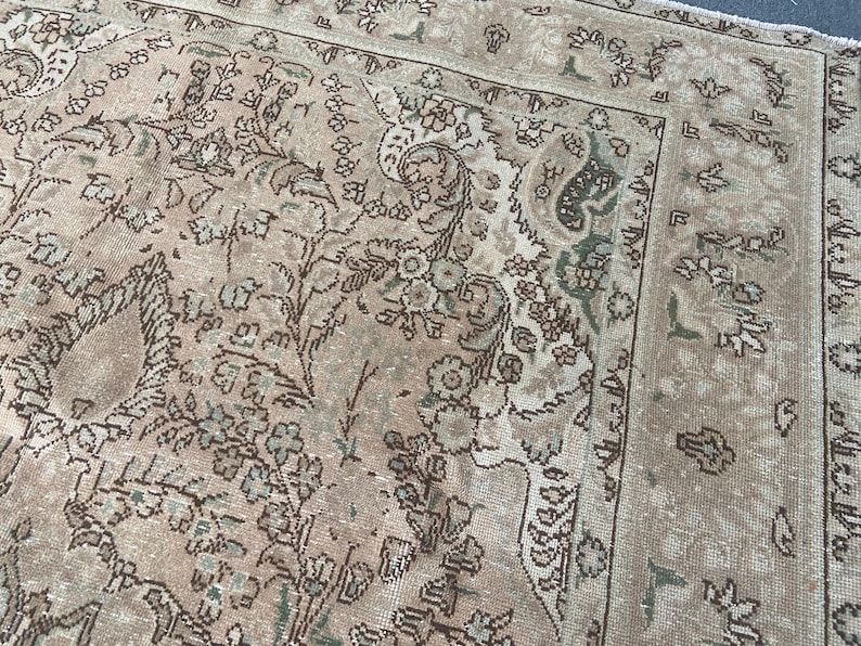 May include: A vintage-style rug with a faded, distressed appearance. The rug features a beige and brown color palette with intricate floral and paisley patterns. The border has a darker brown design, adding contrast to the overall look.