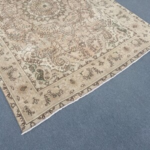 May include: A beige and brown patterned area rug with a detailed floral design. The rug has a central medallion and a border with repeating floral motifs. The rug is placed on a blue surface.