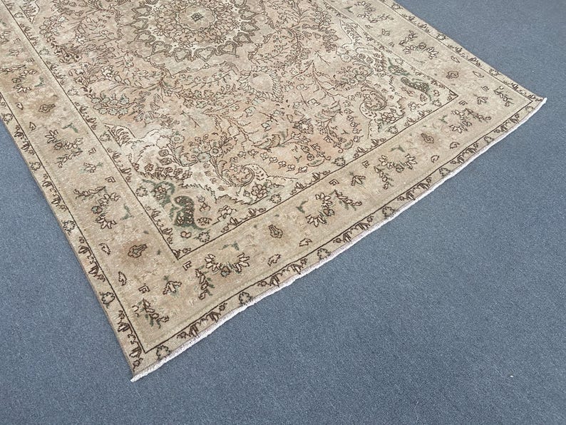 May include: A beige and brown patterned area rug with a detailed floral design. The rug has a central medallion and a border with repeating floral motifs. The rug is placed on a blue surface.