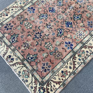 May include: A rectangular, vintage-style rug with a faded, floral pattern in shades of pink, blue, and cream. The rug features a detailed border with floral and geometric designs, adding to its antique aesthetic. The rug's dimensions are not visible.