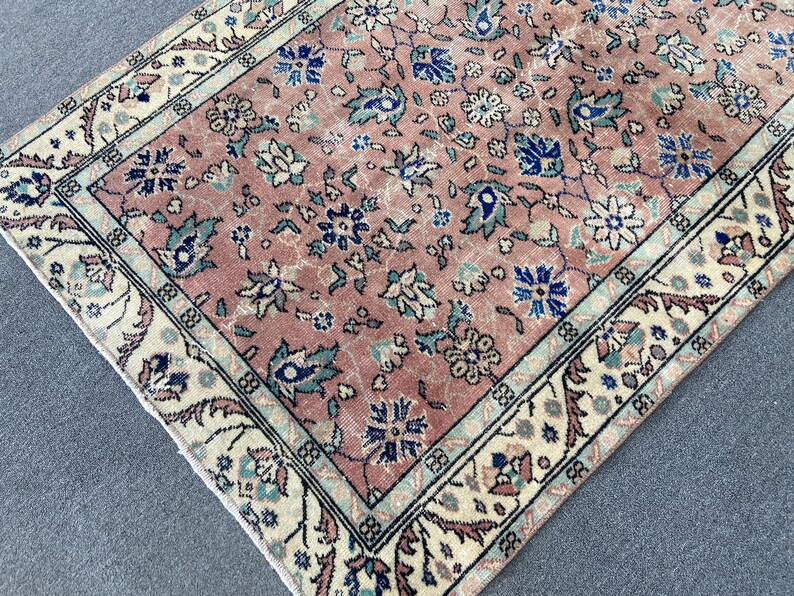 May include: A rectangular, vintage-style rug with a faded, floral pattern in shades of pink, blue, and cream. The rug features a detailed border with floral and geometric designs, adding to its antique aesthetic. The rug's dimensions are not visible.