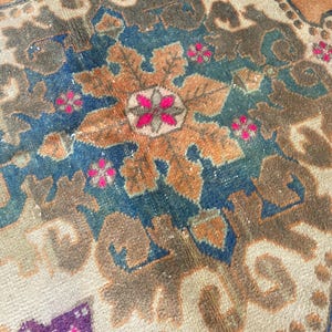 May include: A woven rug featuring a central floral medallion in shades of orange, deep blue, and brown. The design includes intricate geometric patterns and small, vibrant pink flower accents set against a light beige and orange background.