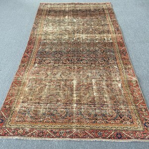 May include: An antique, rectangular rug with a distressed, faded appearance. The rug features a central field of muted colors, including beige, brown, and hints of blue. A detailed border in shades of red and navy frames the rug.