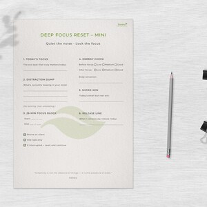 May include: A minimalist planner titled "DEEP FOCUS RESET - MINI" with text and fill-in sections. A gray pencil and two black binder clips are on the right. The planner's text includes "Today's Focus", "Distraction Dump", and "25-Min Focus Block".