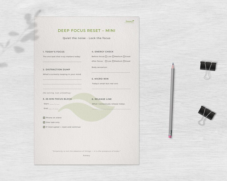 May include: A minimalist planner titled "DEEP FOCUS RESET - MINI" with text and fill-in sections. A gray pencil and two black binder clips are on the right. The planner's text includes "Today's Focus", "Distraction Dump", and "25-Min Focus Block".