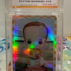 May include: A 2025 Toy Pop Collections trading card featuring Peyton Manning #18, graded Gem Mint 10. The card showcases a stylized figure of Manning in a yellow and white uniform, holding a football. The text "The Sheriff" is at the bottom.