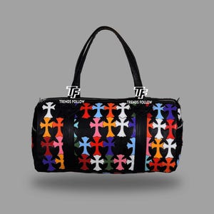 May include: Black duffel bag with a colorful cross pattern. The bag has two black handles and a zipper closure. The crosses are in various colors, including red, blue, orange, and white. The bag has the text "TRENDS FOLLOW" on it.
