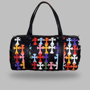 May include: Black duffel bag with a colorful cross pattern. The bag features a zipper closure, two handles, and a rectangular shape. The crosses are in various colors, including red, orange, yellow, pink, blue, and white.