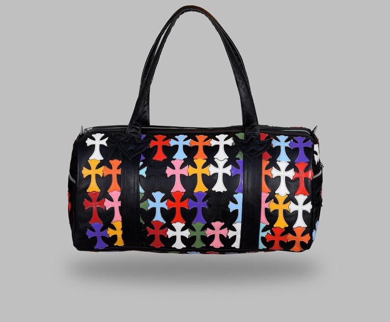 May include: Black duffel bag with a colorful cross pattern. The bag features a zipper closure, two handles, and a rectangular shape. The crosses are in various colors, including red, orange, yellow, pink, blue, and white.