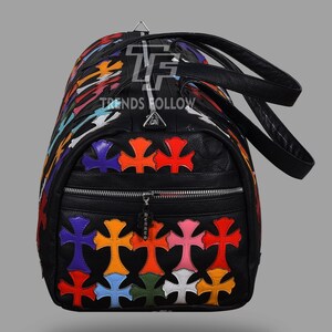 May include: Black duffel bag with colorful cross appliques. The bag features a zippered front pocket and black leather handles. The text "TRENDS HOLLOW" is visible on the bag.