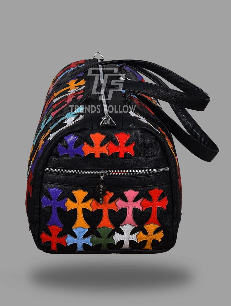 May include: Black duffel bag with colorful cross appliques. The bag features a zippered front pocket and black leather handles. The text "TRENDS HOLLOW" is visible on the bag.