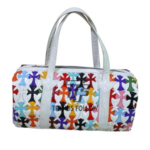 May include: White leather duffel bag with colorful cross pattern. The bag features a zip closure, two top handles, and a decorative cross design in various colors, including red, blue, and yellow. The text "TRENDS FOLLOW" is visible on the bag.