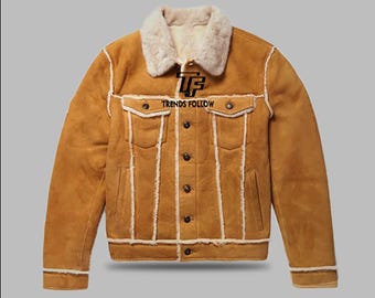 May include: A tan suede jacket with a cream-colored shearling collar and lining. The jacket features a button-up front, two chest pockets, and the text "TRENDS FOLLOW" above the left pocket. The jacket has cream-colored trim.
