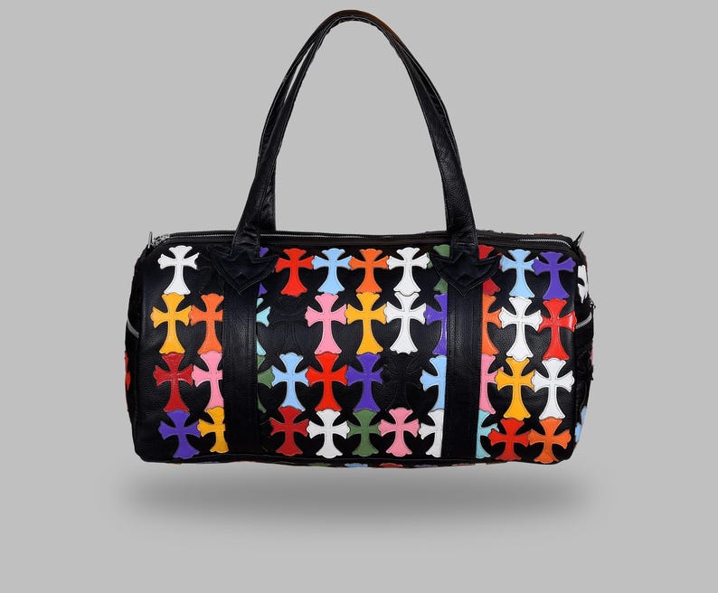 May include: Black duffel bag with a colorful cross pattern. The bag features a zipper closure, two handles, and a vibrant design of multi-colored crosses in red, orange, yellow, pink, blue, green, and white.