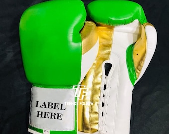 May include: Pair of green and white boxing gloves with gold accents. The gloves have a lace-up closure and a label that says "LABEL HERE". The gloves are made of leather and are designed for boxing.