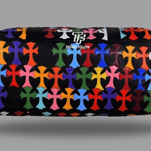 May include: Black leather bag with a pattern of colorful crosses in various shades including orange, blue, green, and pink. The bag has a rectangular shape and a textured surface. The text "TRENDS FOLLOW" is visible on the bag.