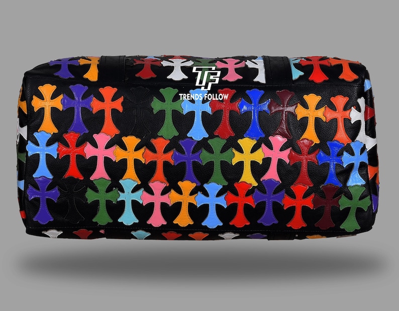May include: Black leather bag with a pattern of colorful crosses in various shades including orange, blue, green, and pink. The bag has a rectangular shape and a textured surface. The text "TRENDS FOLLOW" is visible on the bag.
