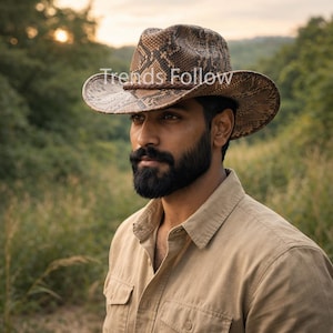 May include: A cowboy hat with a snakeskin pattern. The hat is brown and tan with a dark brown band. The image also shows a tan button-down shirt. The text "Trends Follow" is visible on the hat.