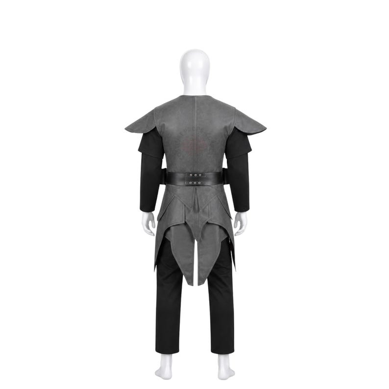 May include: A gray sleeveless tunic with structured shoulder caps and a black belt, worn over a black long-sleeved shirt and black trousers. The tunic features a layered, pointed hemline that extends down the back, creating a distinct silhouette.