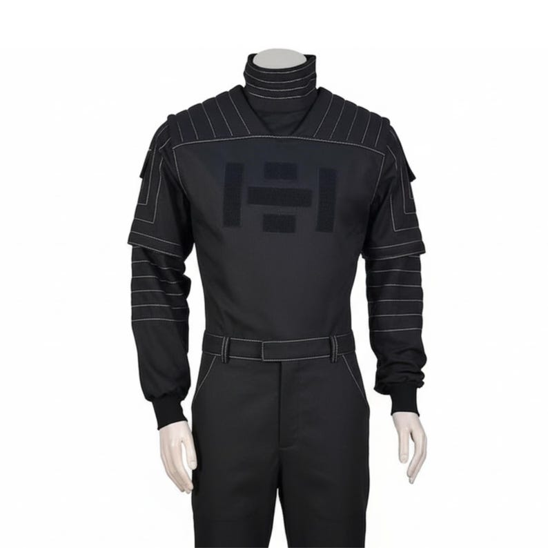 Pu&ograve; includere: Tuta nera con collo alto e maniche lunghe. L'outfit presenta dettagli di cuciture bianche e una cintura. Un grande emblema scuro &egrave; centrato sul petto. Le maniche hanno un design a strati.