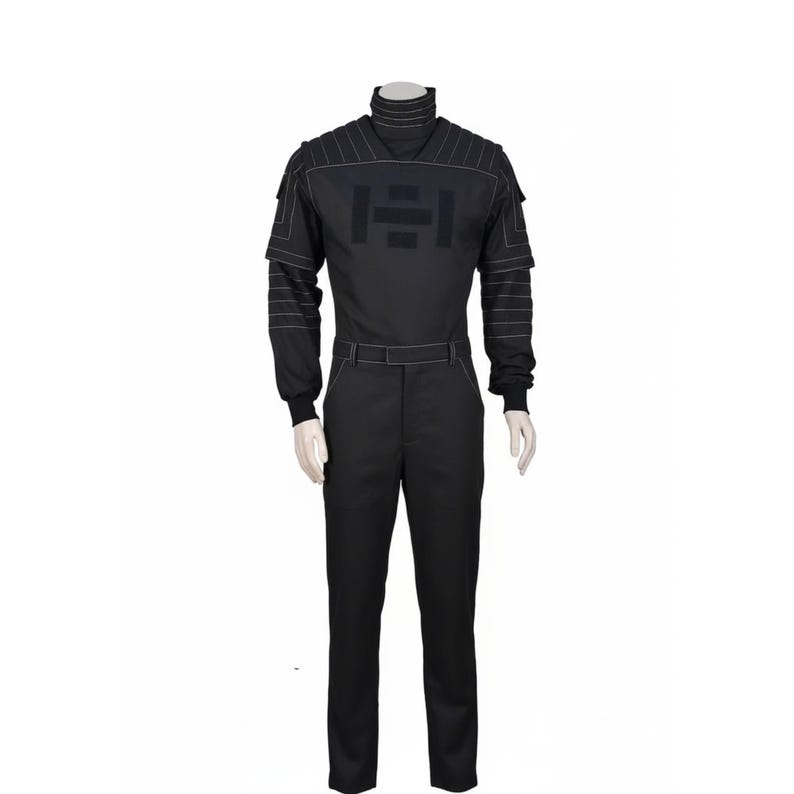 Pu&ograve; includere: Tuta nera con collo alto e maniche lunghe. La tuta presenta dettagli di cucitura bianchi sulle spalle e sulle maniche e una grande grafica sul petto. I pantaloni hanno una cintura e sono a gamba dritta.