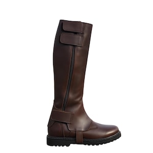 May include: A tall, brown leather boot with a black sole. The boot features a side zipper and two adjustable straps at the top and one at the ankle. The boot is designed for riding or equestrian activities.