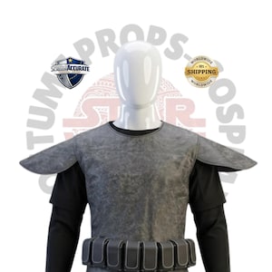 May include: A gray textured chest armor piece with wide shoulder pauldrons worn over a black long-sleeved shirt. A utility belt with multiple rectangular pouches is fastened at the waist. The armor has a weathered appearance and a round neckline.