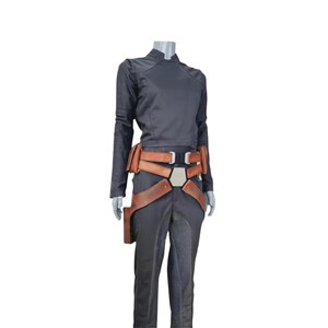 K&ouml;nnte beinhalten: Ein schwarzes Cosplay-Kost&uuml;m mit einem lang&auml;rmeligen Oberteil und einer Hose. Das Kost&uuml;m enth&auml;lt einen braunen Lederg&uuml;rtel mit mehreren Riemen und eine Halterung. Das Outfit wird auf einer Schaufensterpuppe pr&auml;sentiert.