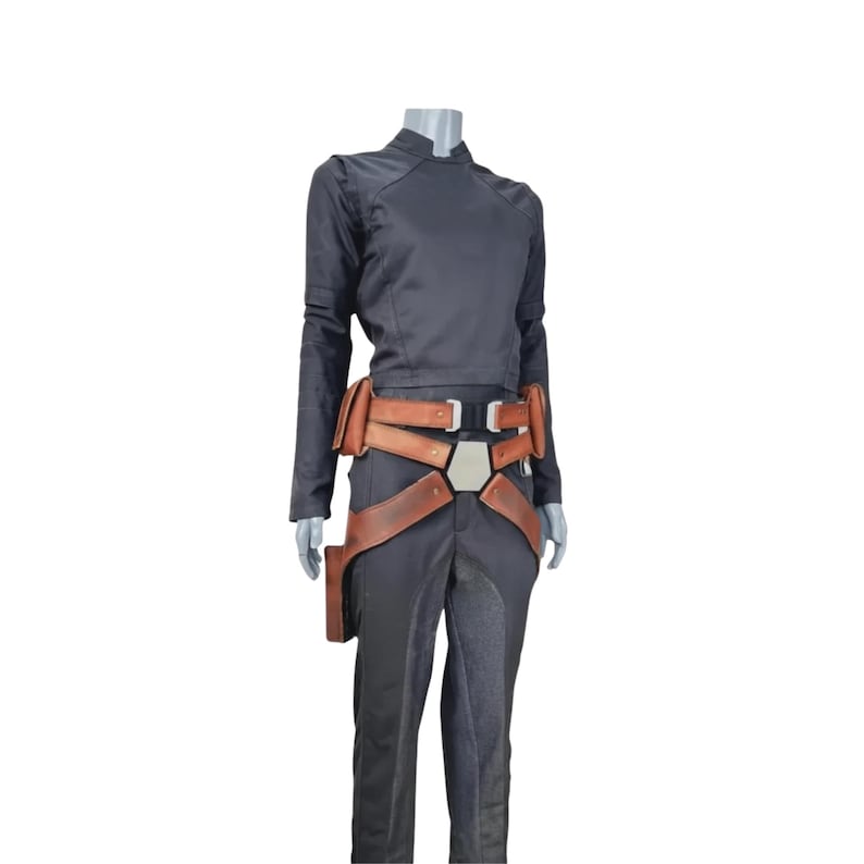 K&ouml;nnte beinhalten: Ein schwarzes Cosplay-Kost&uuml;m mit einem lang&auml;rmeligen Oberteil und einer Hose. Das Kost&uuml;m enth&auml;lt einen braunen Lederg&uuml;rtel mit mehreren Riemen und eine Halterung. Das Outfit wird auf einer Schaufensterpuppe pr&auml;sentiert.