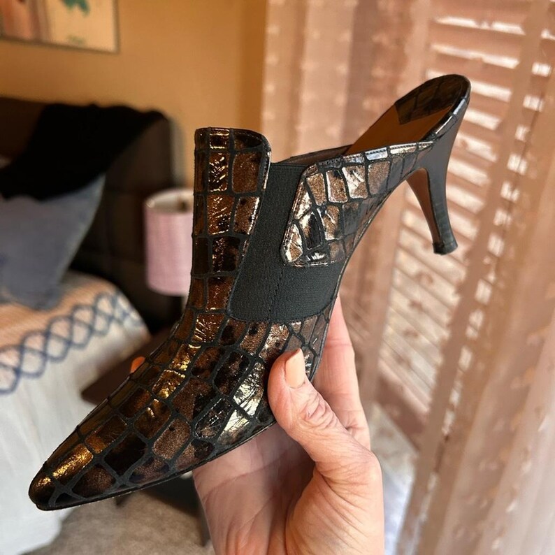 K&ouml;nnte beinhalten: Braune und schwarze Stiefelette mit spitzer Zehenpartie und strukturiertem, krokodilartigem Muster. Die Stiefelette hat einen schwarzen elastischen Einsatz an der Seite und einen Stiletto-Absatz. Der Schuh ist ca. 10 cm hoch.